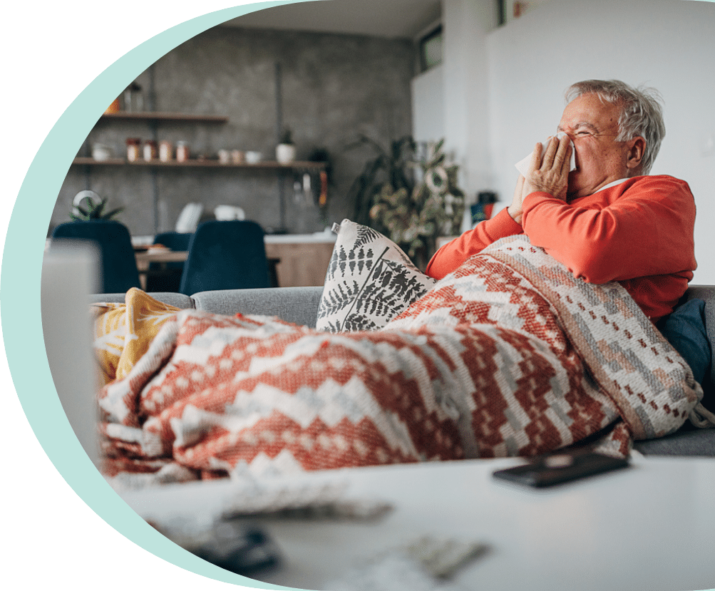 elder man sitting on his couch while sneezing and suffering from pneumonia in seniors