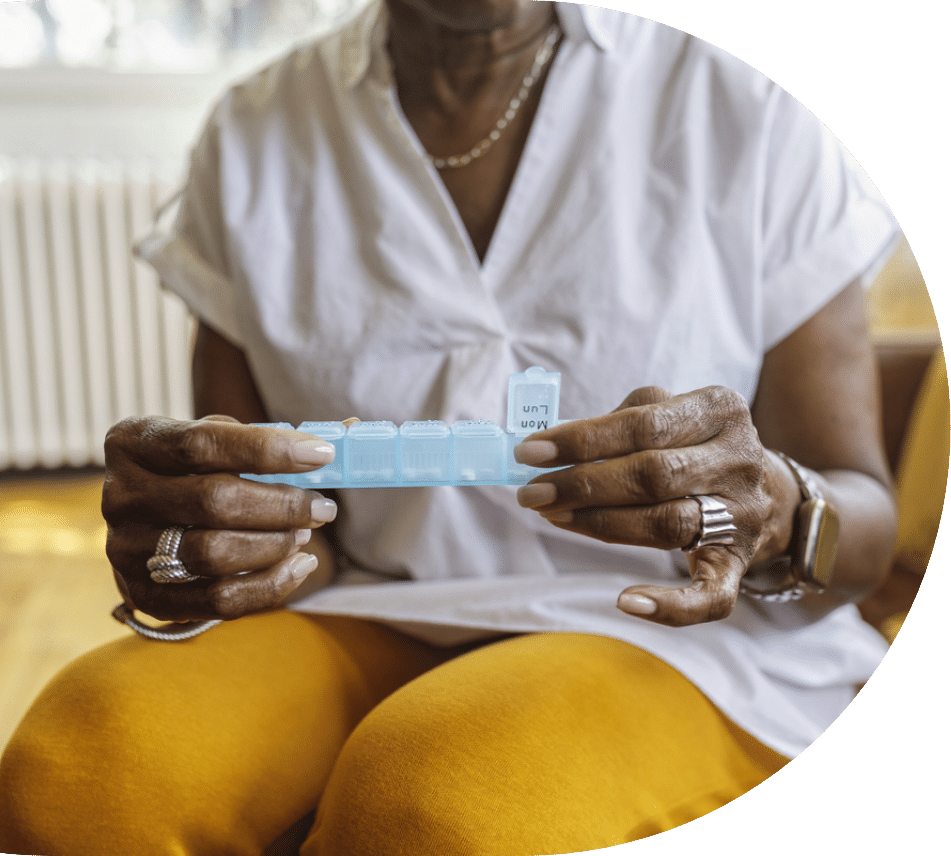 Older woman holding a weekly medication organizer that has an atorvastatin prescription