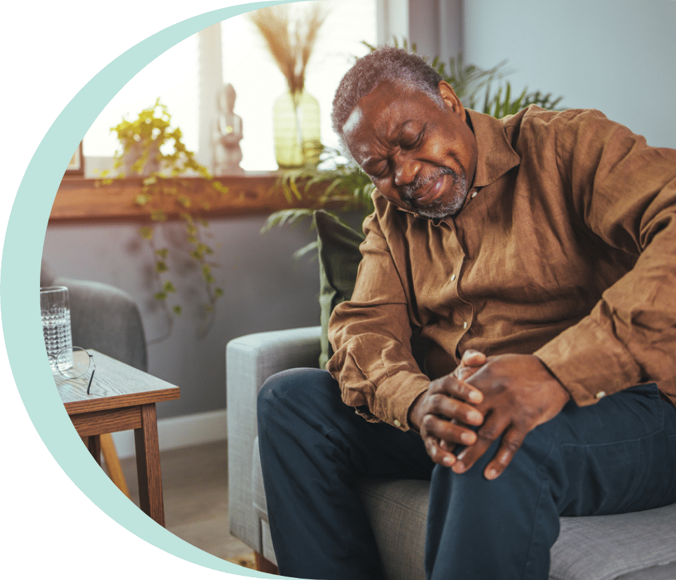 Older man sitting on the couch while holding his leg in pain due to peripheral arterial disease in seniors